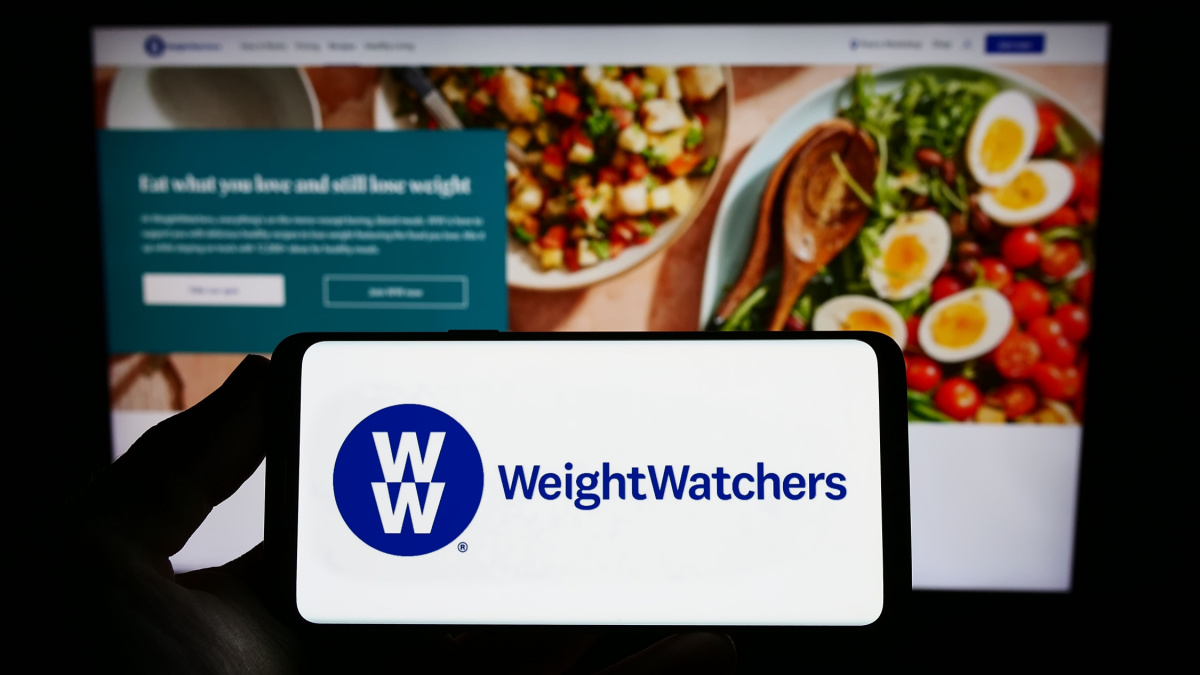 Person holding smartphone with logo of WW International Inc. (Weight Watchers) on screen in front of website.