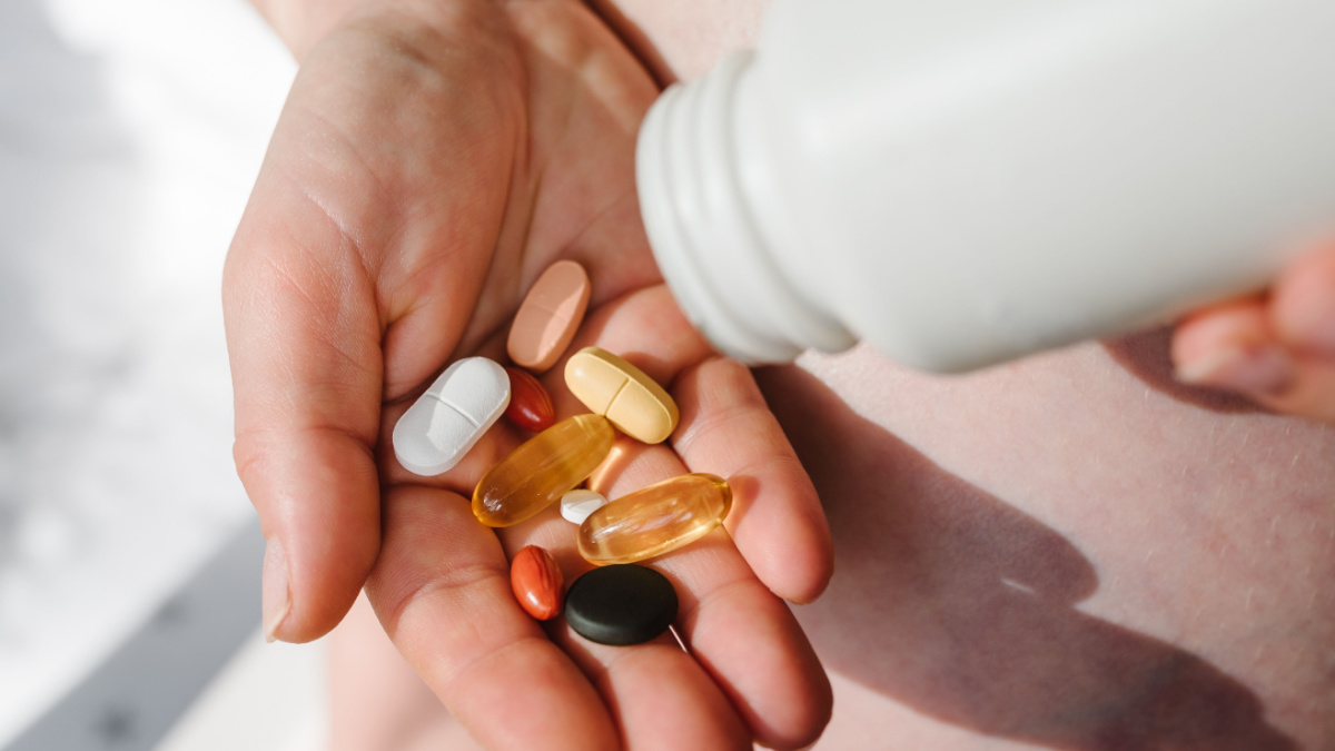 Closeup photo of supplements with a white bottle. Pregnant woman take omega 3, multivitamins, vitamins B, C, D, collagen tablets, probiotics, iron capsule. Girl hold vitamins daily.