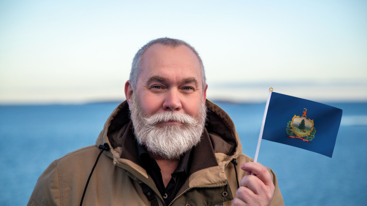 Man holding Vermont state flag. Portrait of older man with Vermont flag. Visit Vermont. Older man 50 55 60 years old with gray beard outdoors traveling.