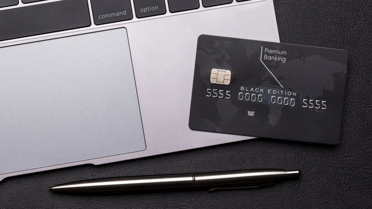 Black credit card on office table with laptop and pen. Flat lay. Premium banking concept