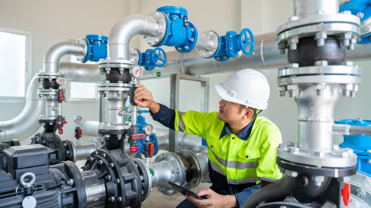 A worker at a water supply station inspects water pump valves equipment in a substation for the distribution of clean water at a large industrial estate. Water pipes. Industrial plumbing.