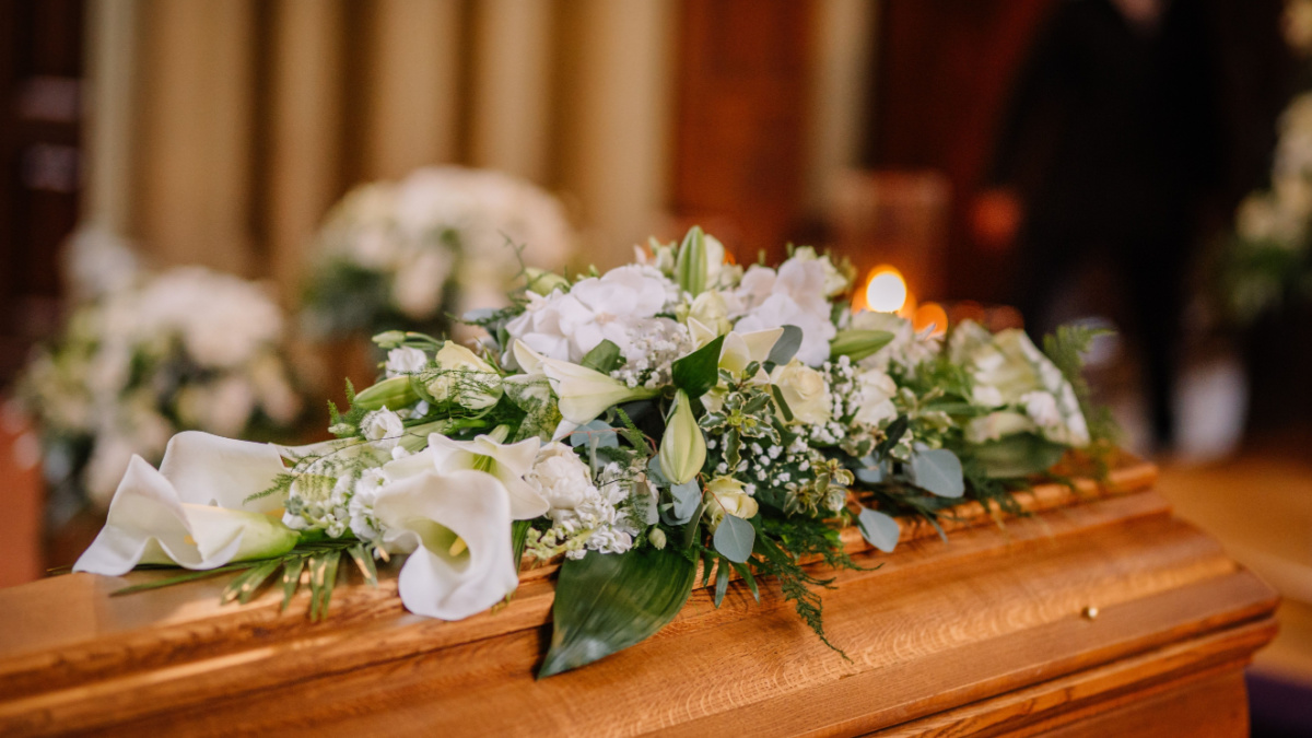 A coffin decorated with many flowers and candles in a beautiful church, ceremony.