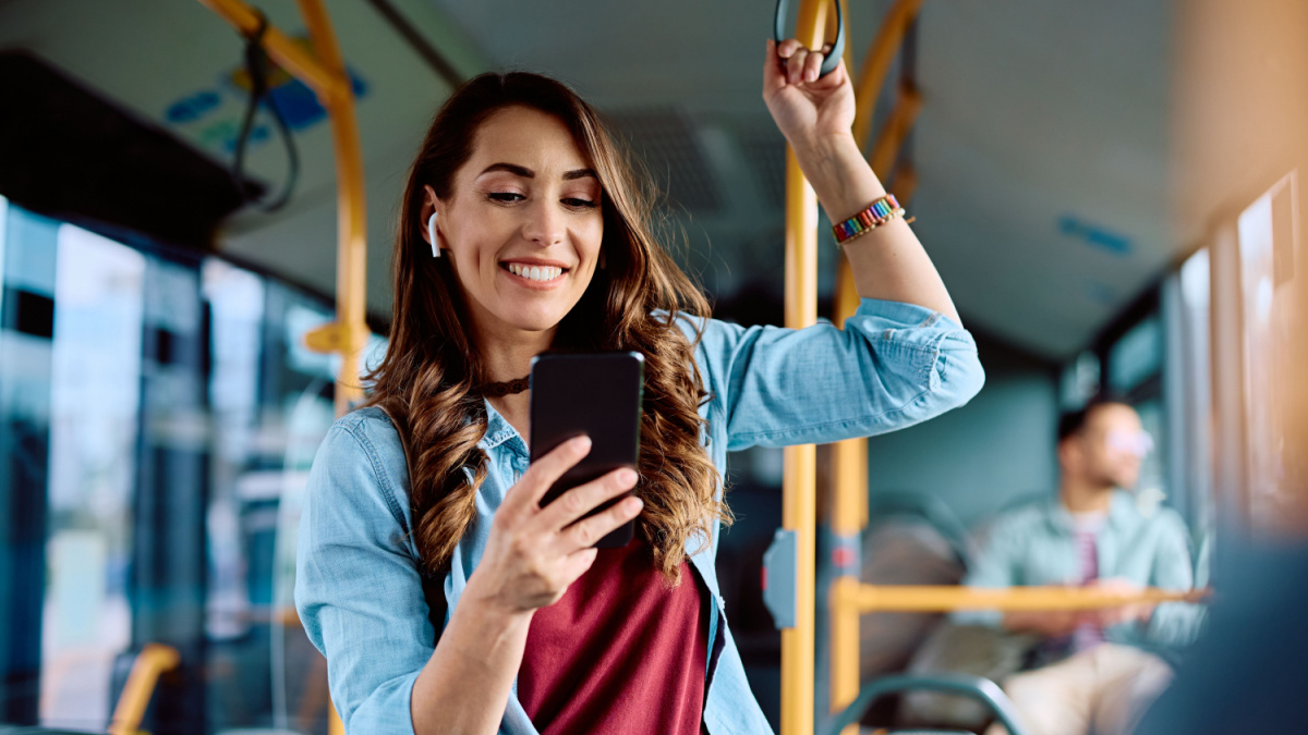 Happy woman text messaging on mobile phone while riding in a bus.