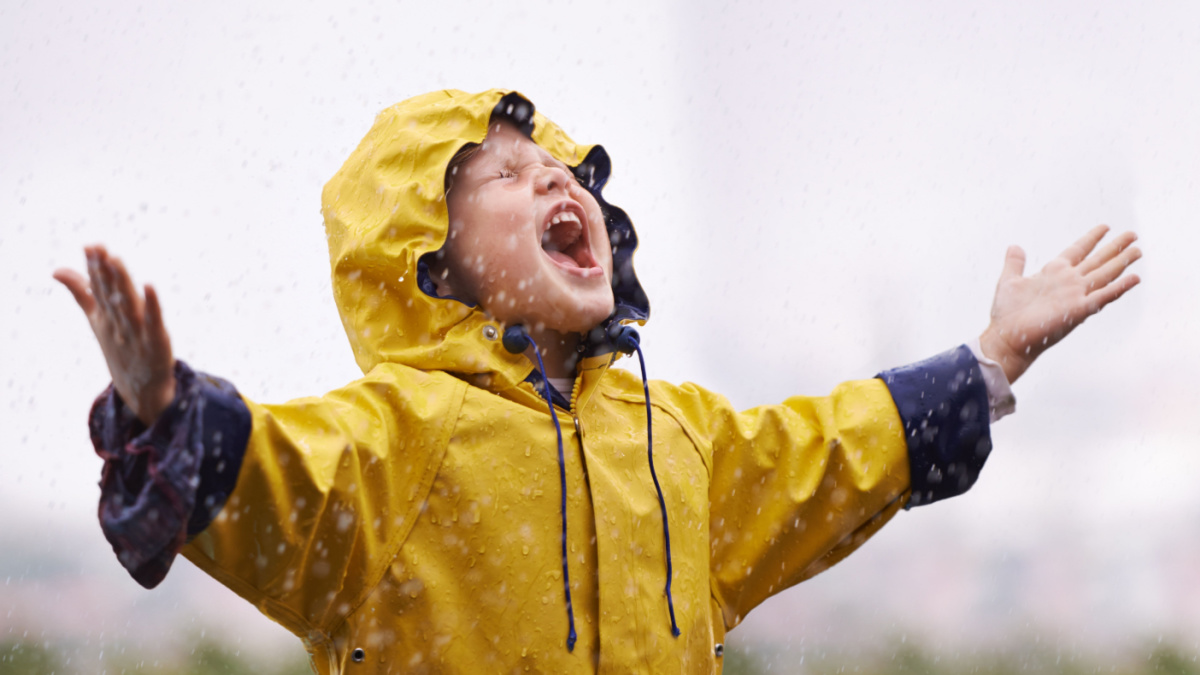 Girl, playing outdoor and screaming in rain, nature and excited with winter fashion. Female child, raincoat and playful with water, open hands and happiness on adventure with freedom in childhood