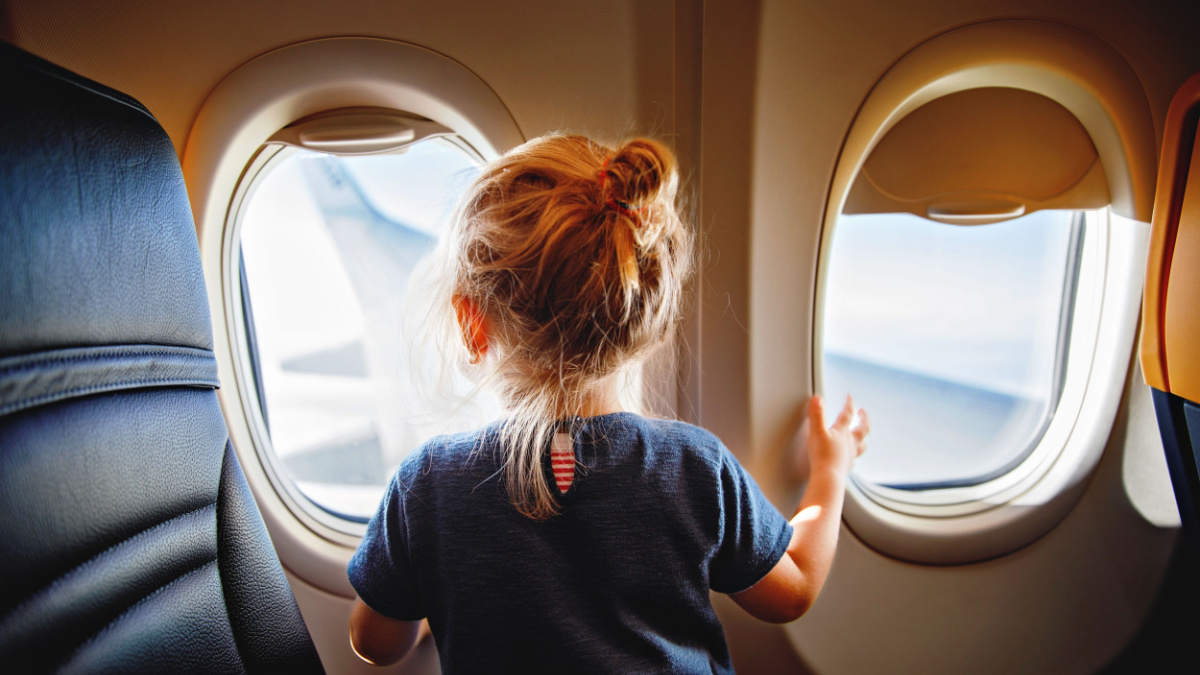 Adorable little girl traveling by an airplane. Child sitting by aircraft window and looking outside. Traveling with kids abroad. Family on summer vacations.