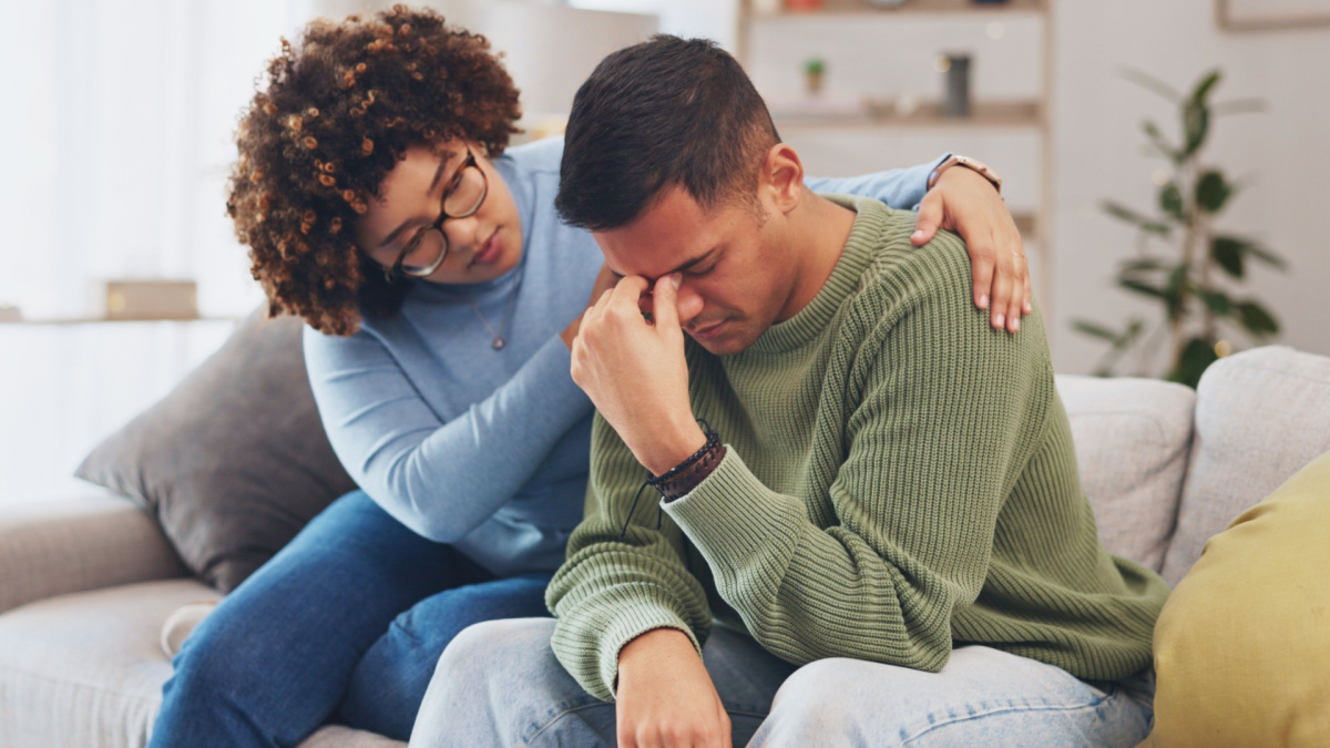 Grief, loss with mental health and sad, stress and people in relationship in crisis. Couple, depression and woman comfort man with empathy, support and love while sitting in living room at home.