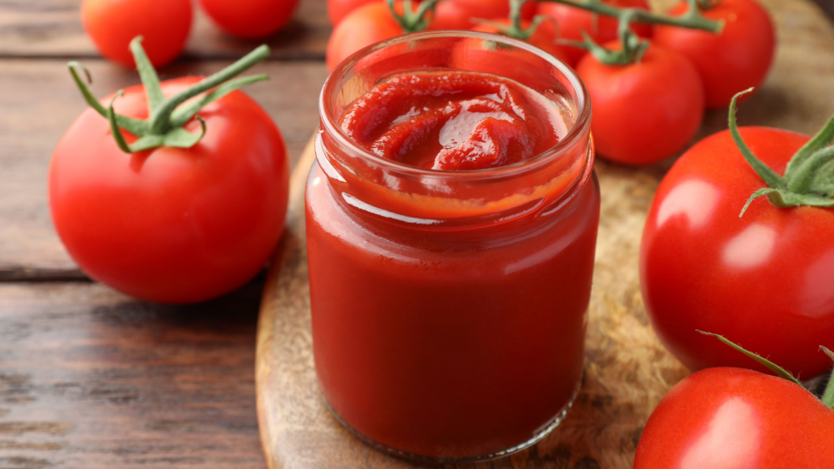 Jar of tasty ketchup and tomatoes on wooden table