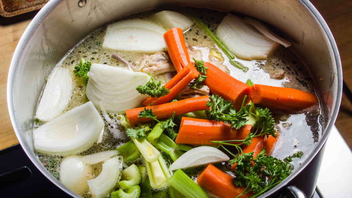 A large stock pot on a stove with vegetables cut for making soup.