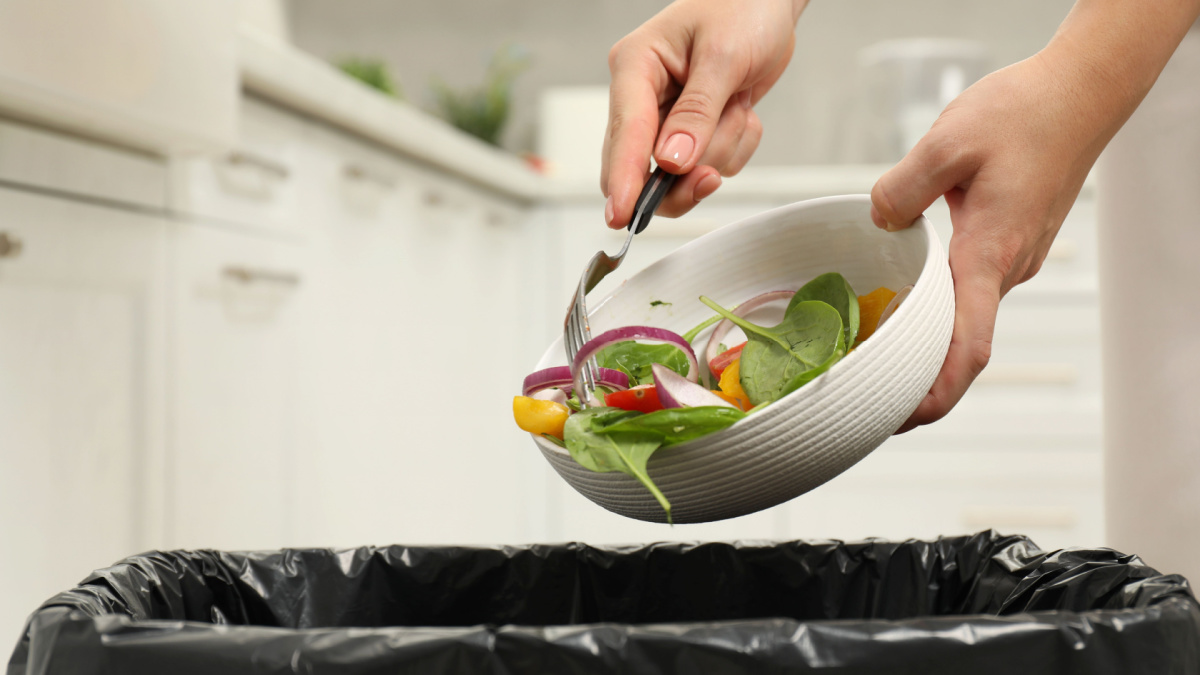 Woman throwing vegetable salad into bin