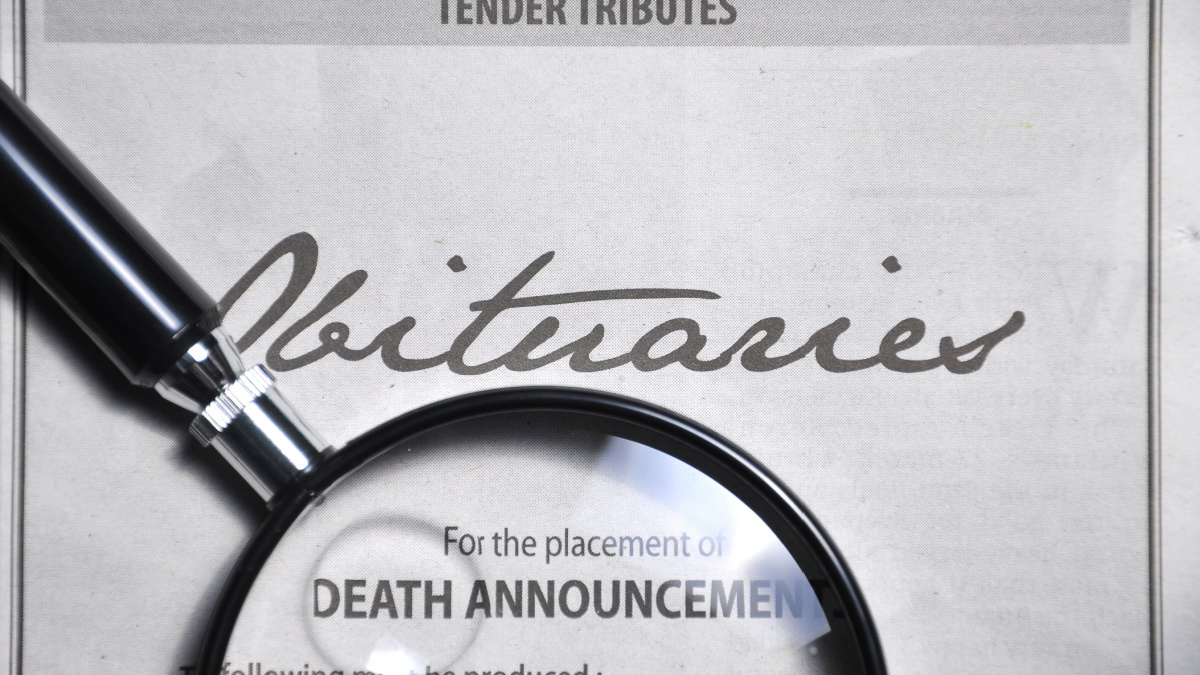 magnifying glass and obituaries advertisement on newspaper.