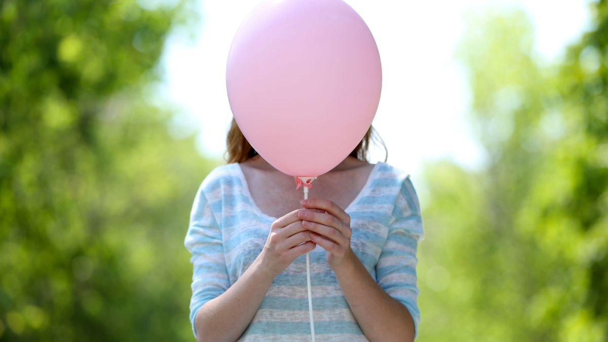 Girl holding balloon near face.