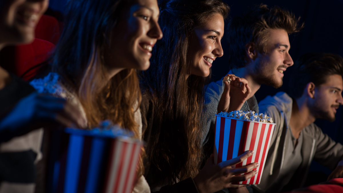 Group of teenager friends at the cinema watching a movie together and eating popcorn, entertainment and enjoyment concept