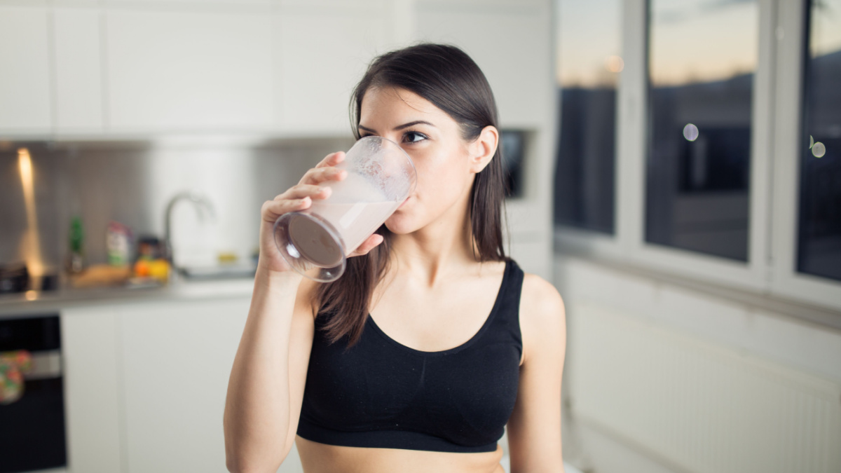Woman in sportswear drinking sweet banana chocolate protein powder milkshake smoothie.Drinking protein after workout.Whey,banana and low fat milk sport nutrition diet after gym.Healthy lifestyle