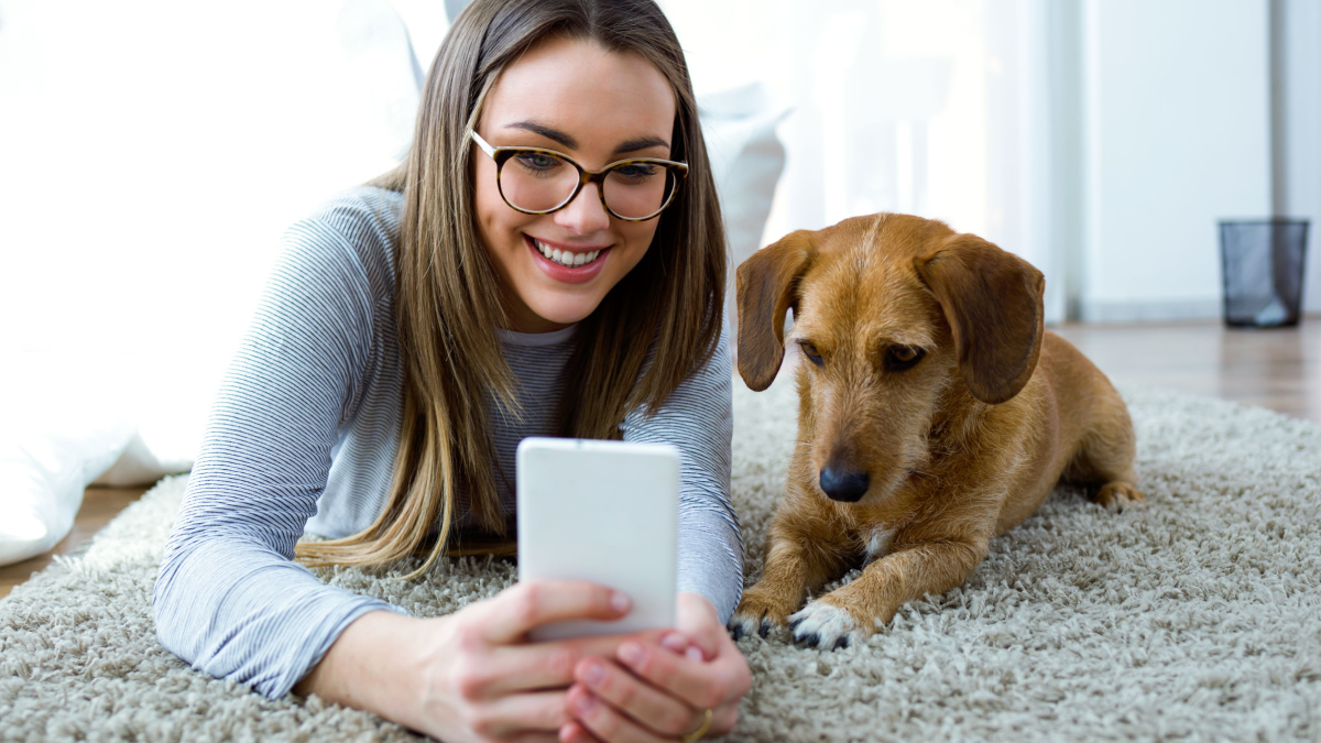 Portrait of beautiful young woman with her dog using mobile phone at home.