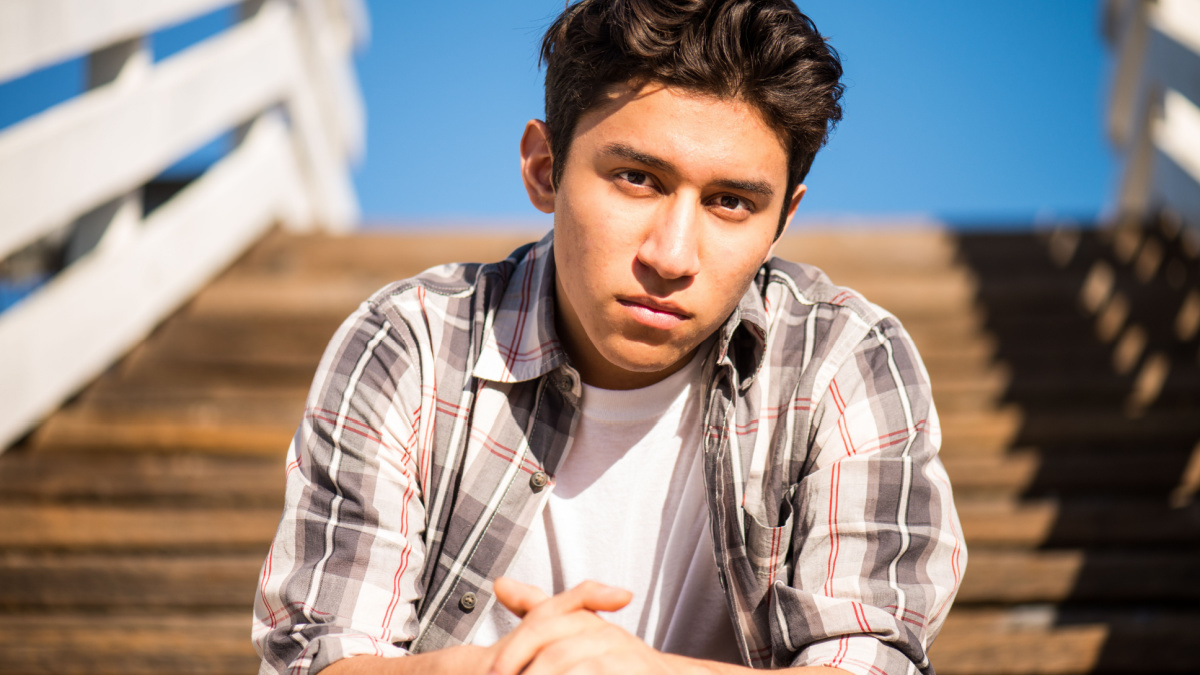 Handsome teenager outdoors, sitting on steps, thinking.