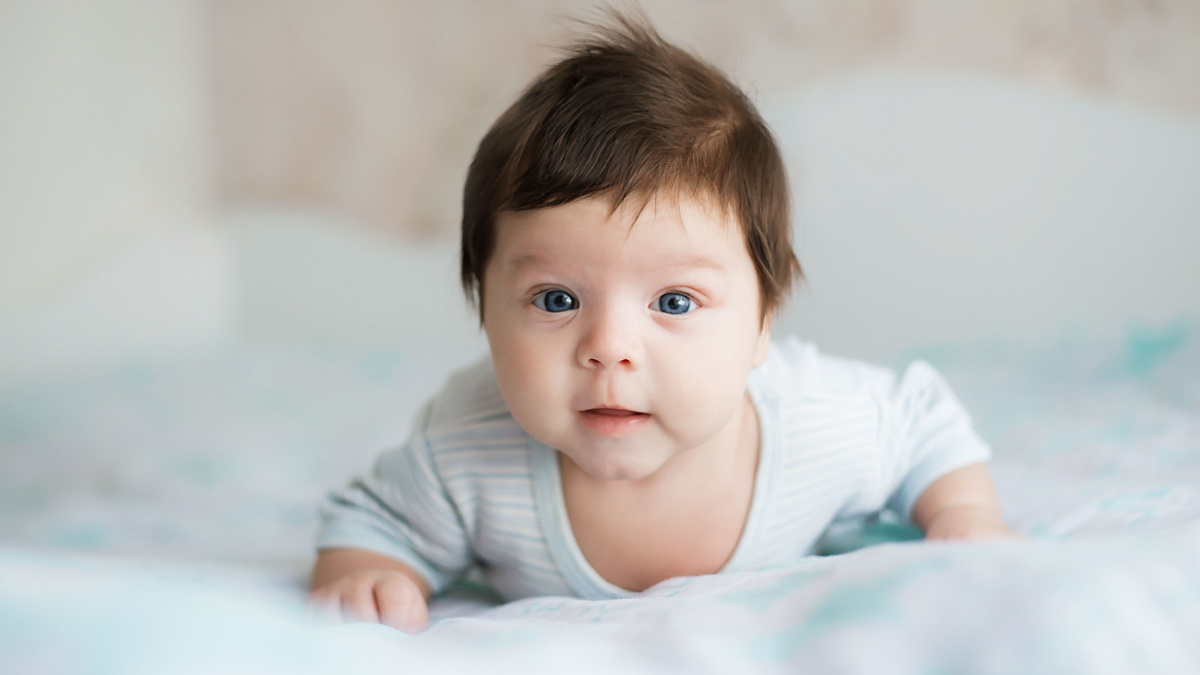 baby, newborn baby cute blue-eyed, dark hair, baby 2 months in a blue body lying on his stomach