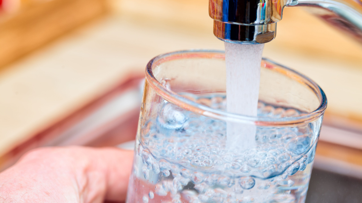 Closeup shot of a man pouring a glass of fresh water from a kitchen faucet.