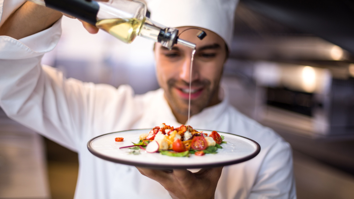 Handsome chef pouring olive oil on meal in a commercial kitchen