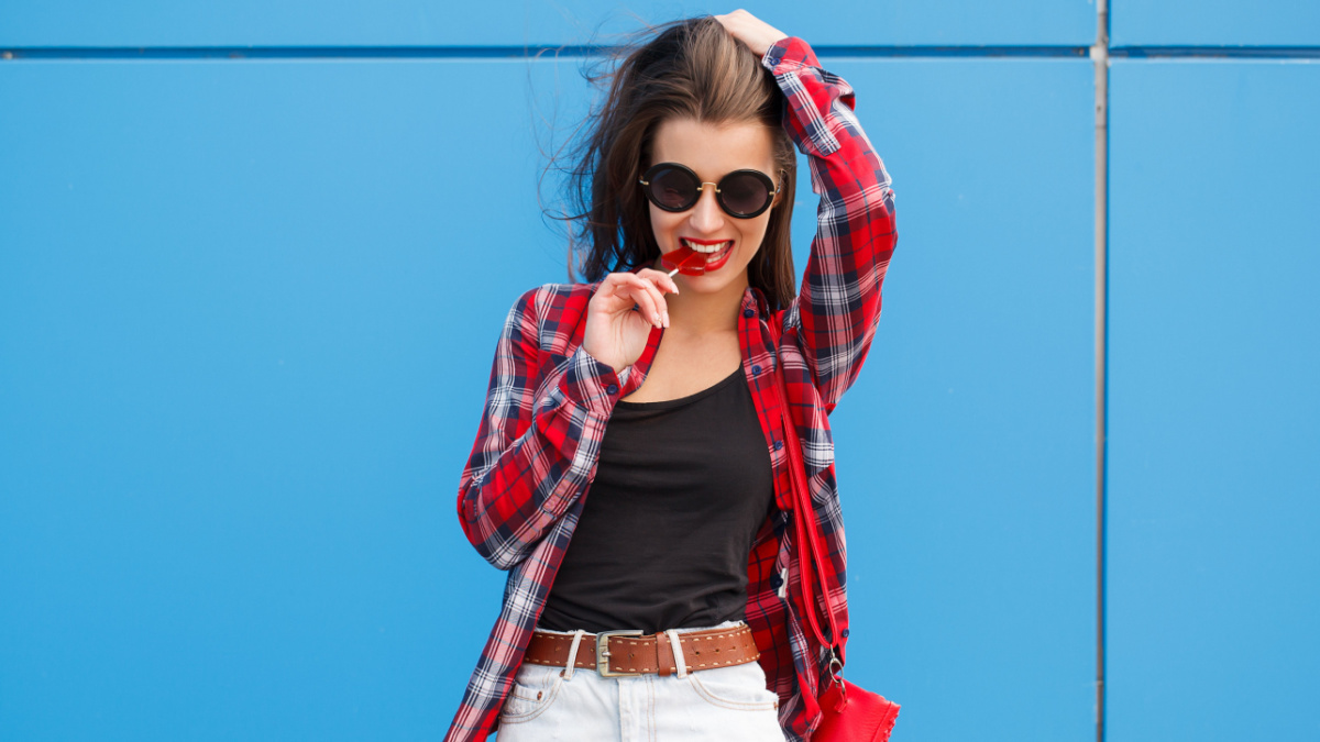 Fashion portrait of pretty smiling woman in sunglasses with lollipop against the colorful blue wall. outdoor.