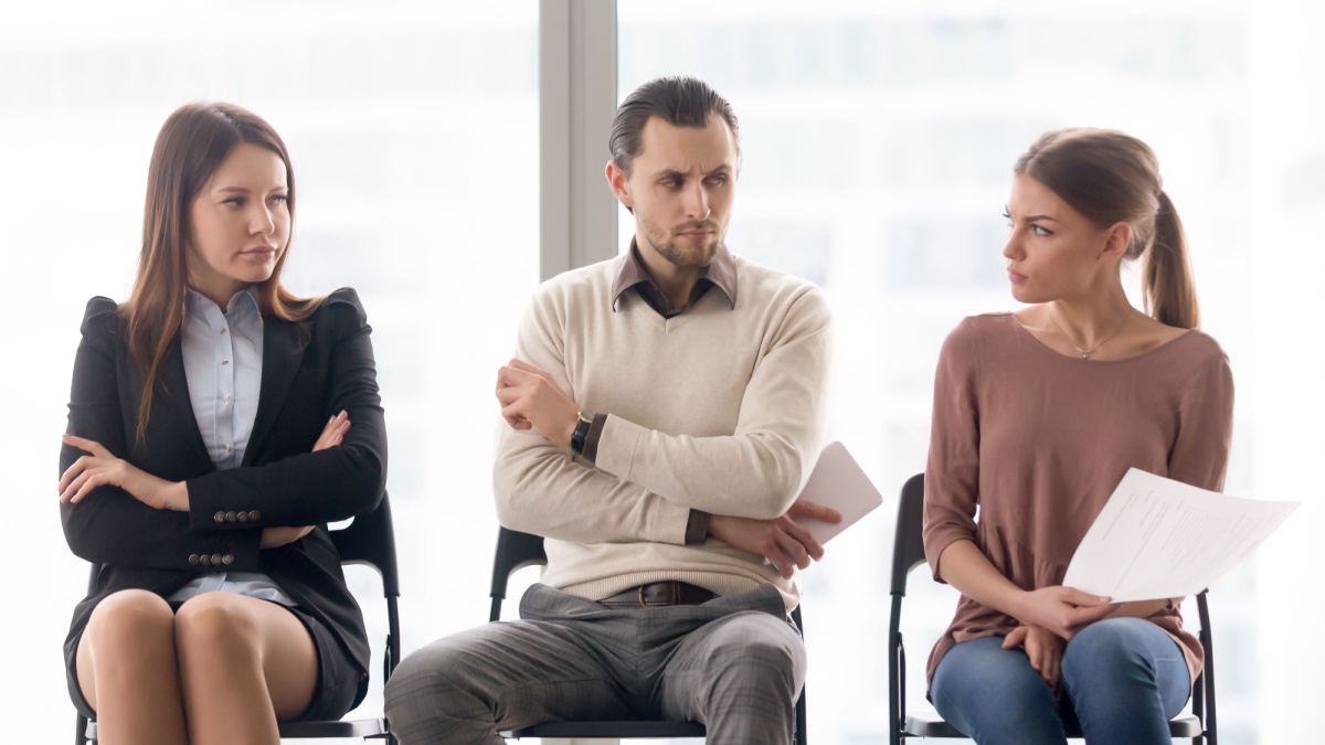 Male and female candidates waiting for interview, sitting together in a row, looking at each other with hate and dislike, feeling jealous envious, rivalry and competition while applying for a job