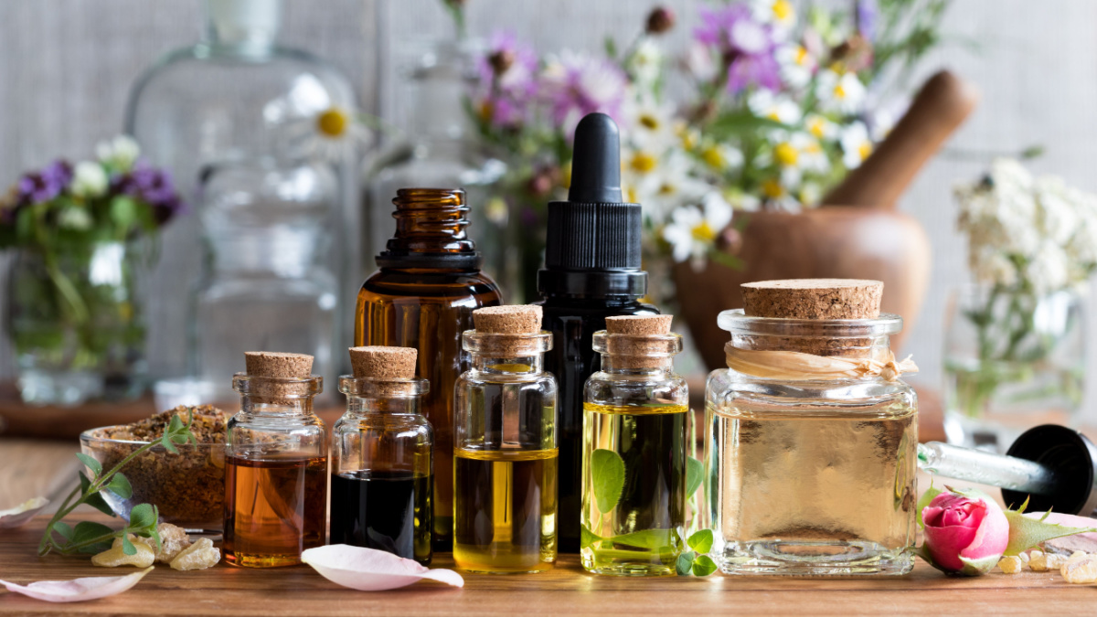 Selection of essential oils, with herbs and flowers in the background