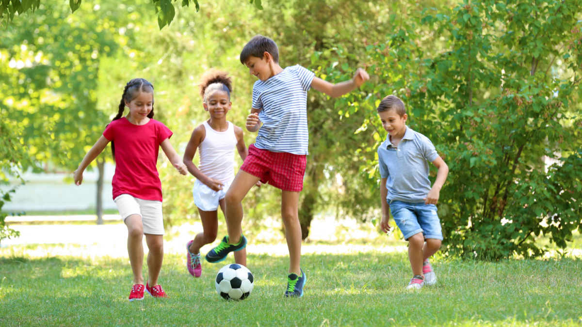 Cute children playing football in park.
