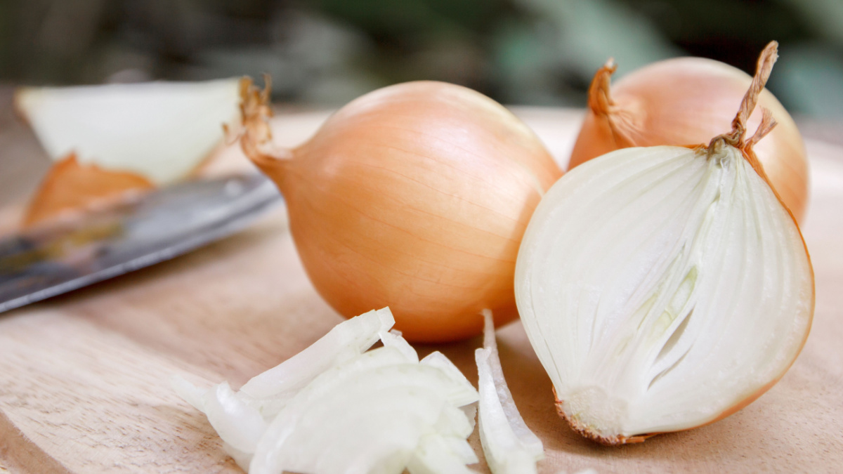 Onion and slices on wooden cutting board.