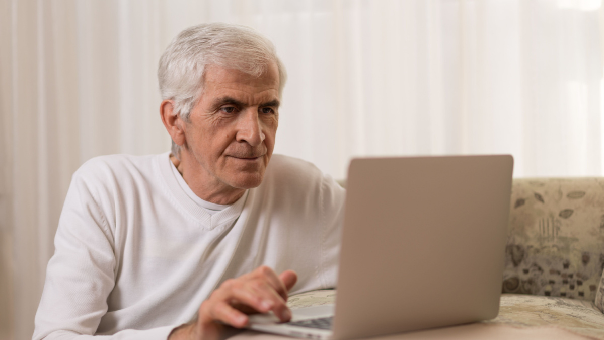 Mature man relaxing on the sofa and typing an e-mail on laptop