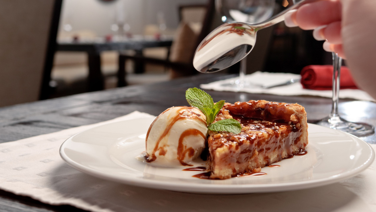 A piece of caramel cake with a scoop of ice-cream decorated with mint leaf on a white plate in a restaurant