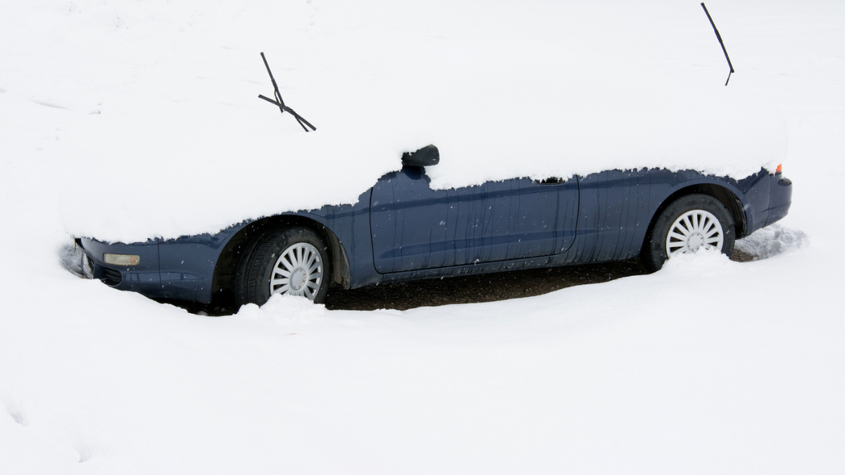 Car covered and surrounded by snow drifts after a snow storm.