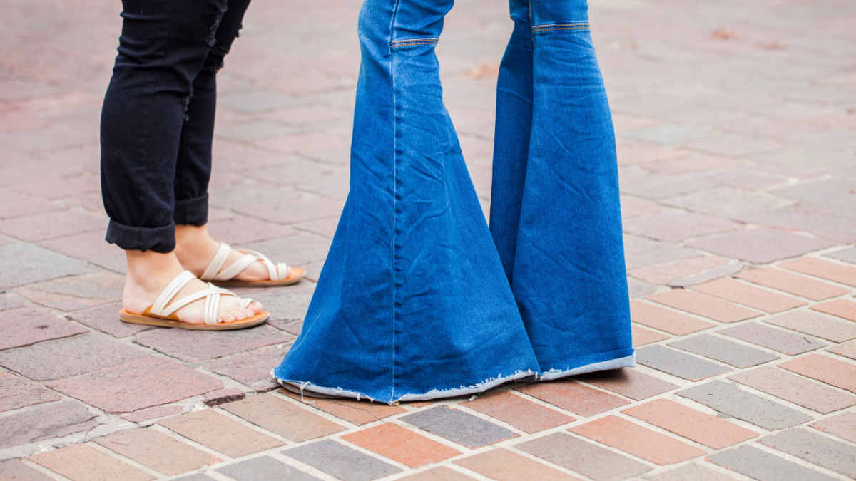 Legs of two girls, one wears seventie's style bell bottom jeans, the other one sandals and modern ripped jeans
