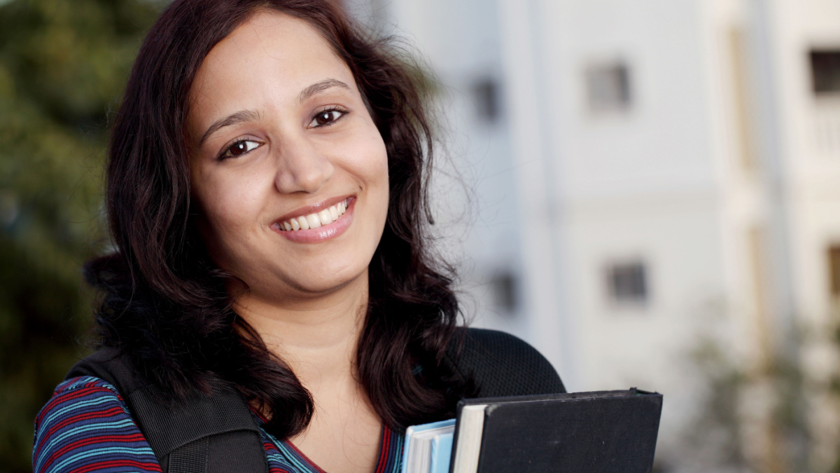 Smiling female student holding text books.