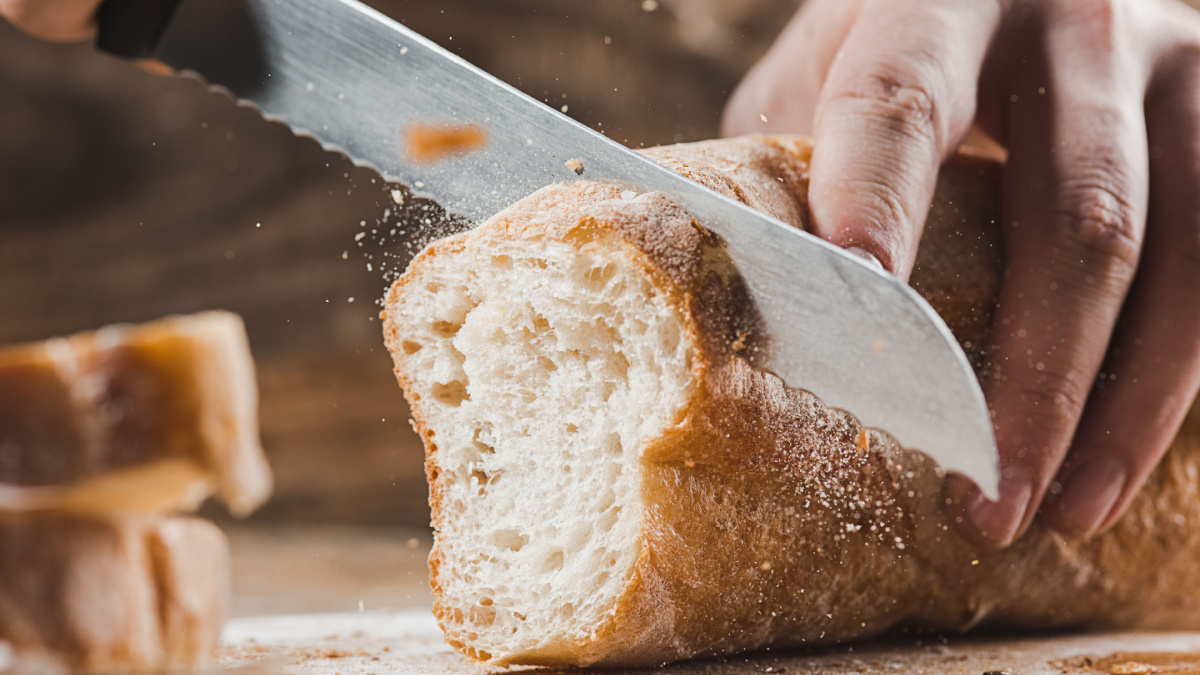 Whole grain bread put on kitchen wood plate with a chef holding gold knife for cut. Fresh bread on table close-up. Fresh bread on the kitchen table The healthy eating and traditional bakery concept