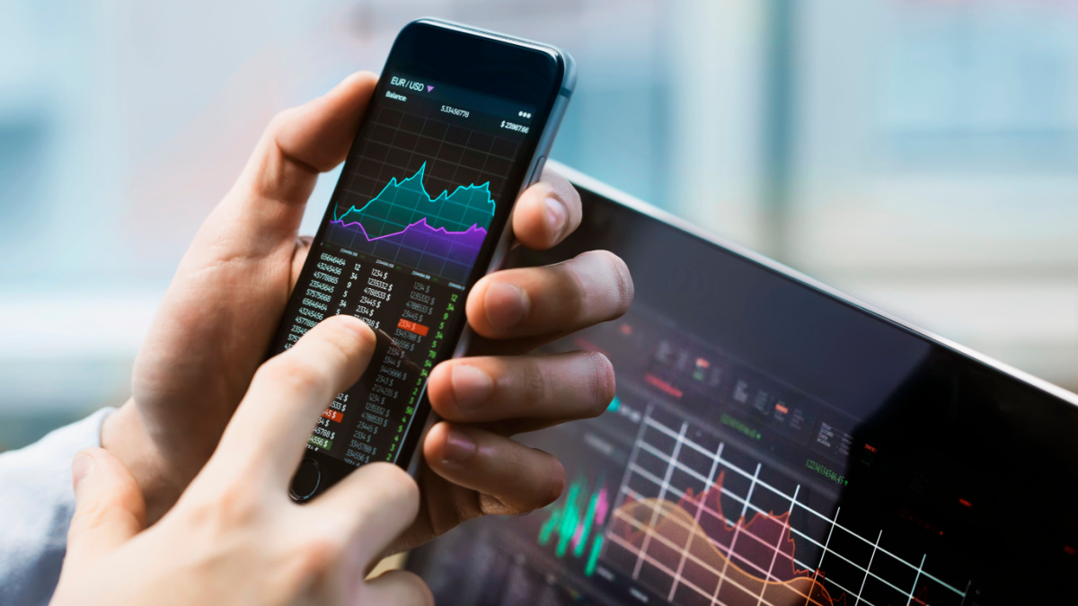 Business man holding phone trading stocks.