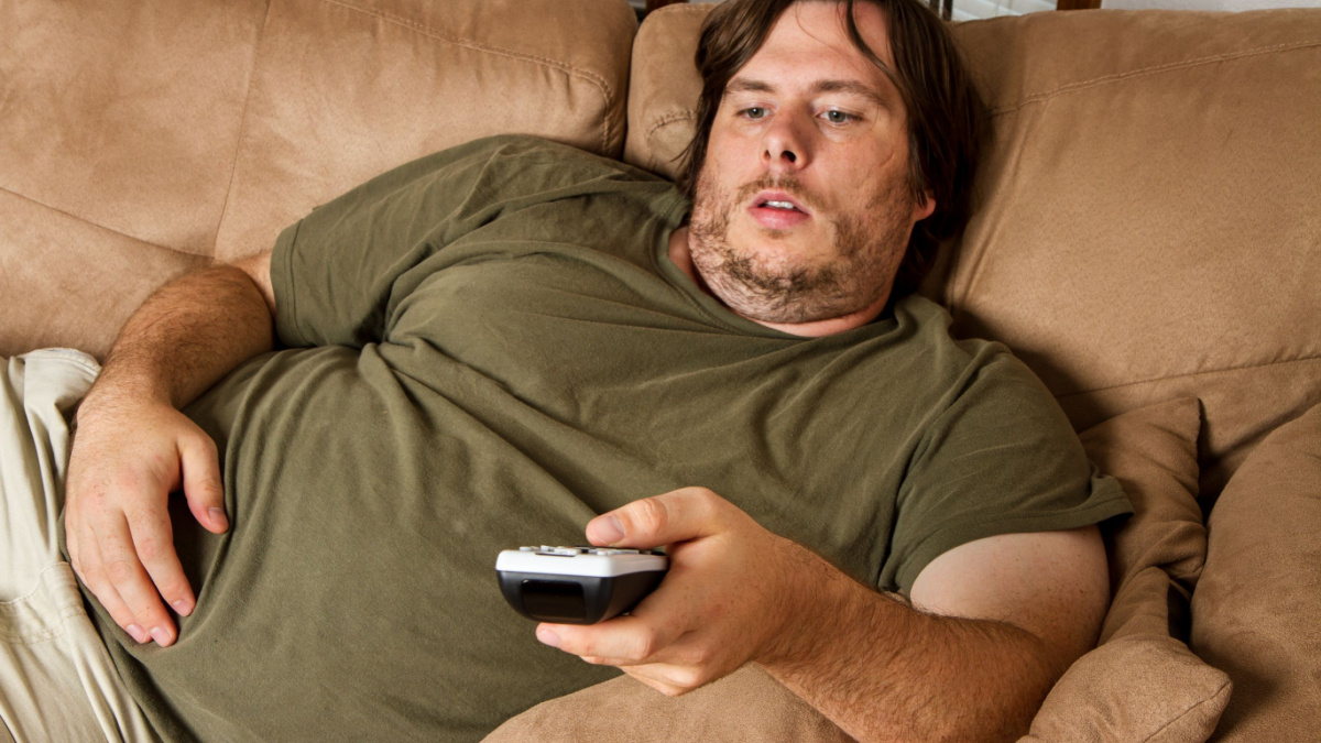 Overweight guy sitting on the couch with remote in hand trying to watch some TV.