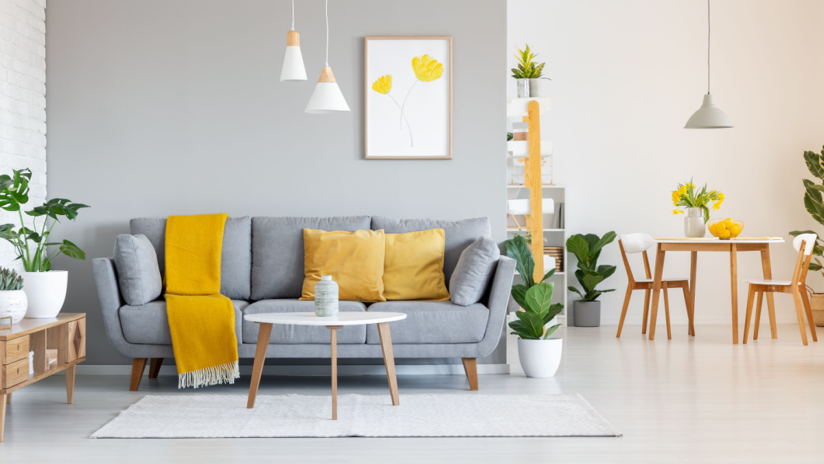 Orange blanket on grey sofa in modern apartment interior with poster and wooden table.