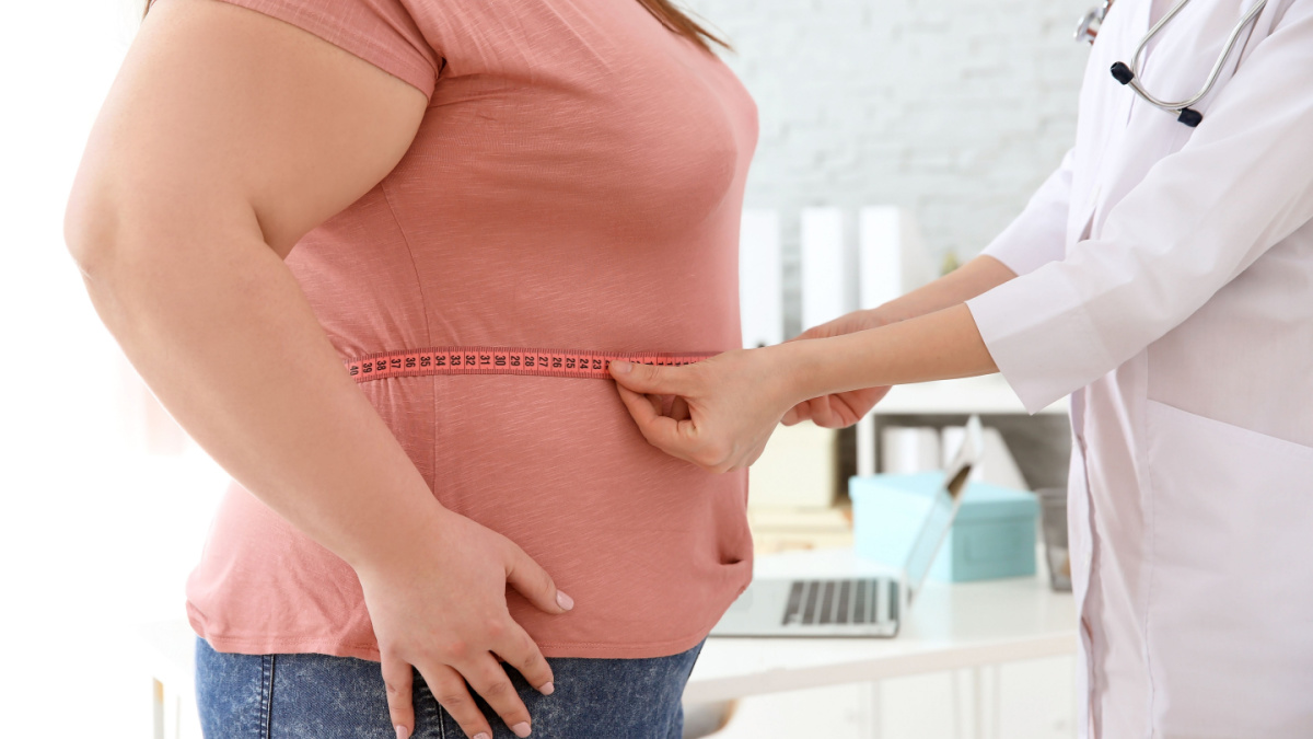 Female doctor measuring waist of overweight woman with measuring tape in clinic