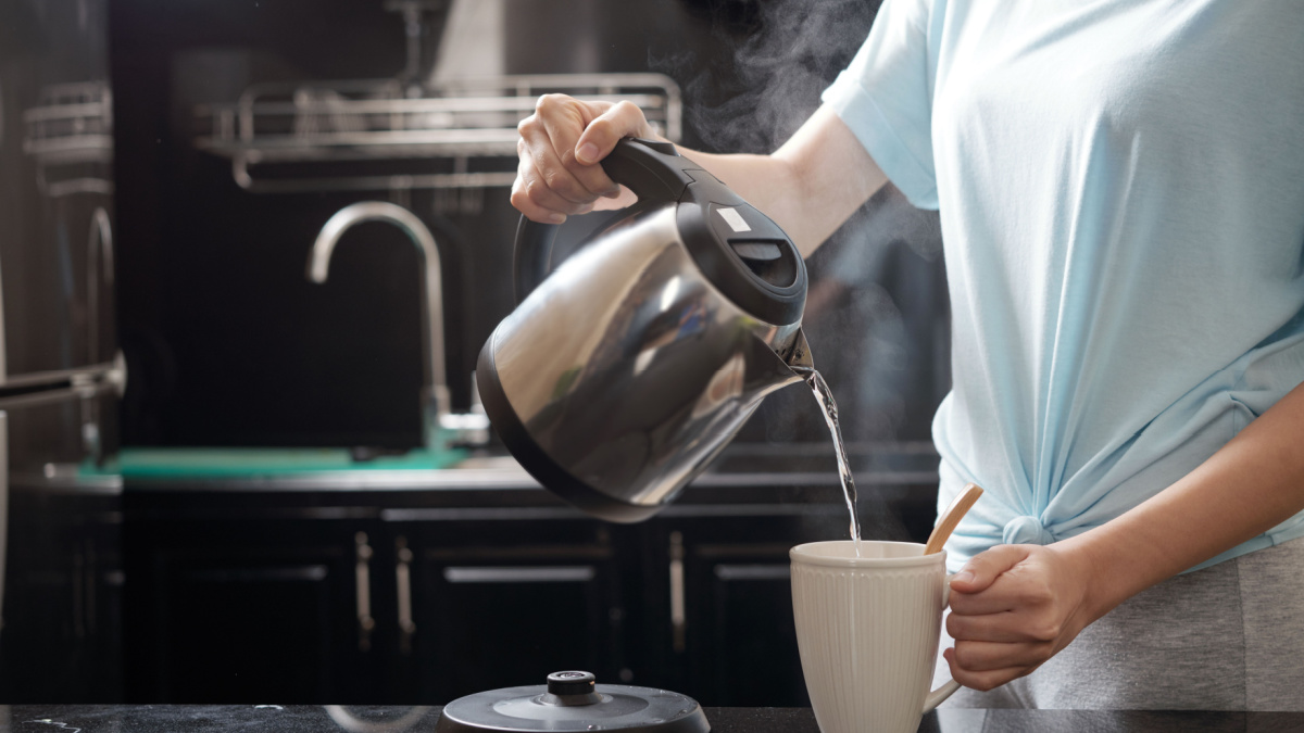 Anonymous female filling mug with hot water while brewing beverage in kitchen