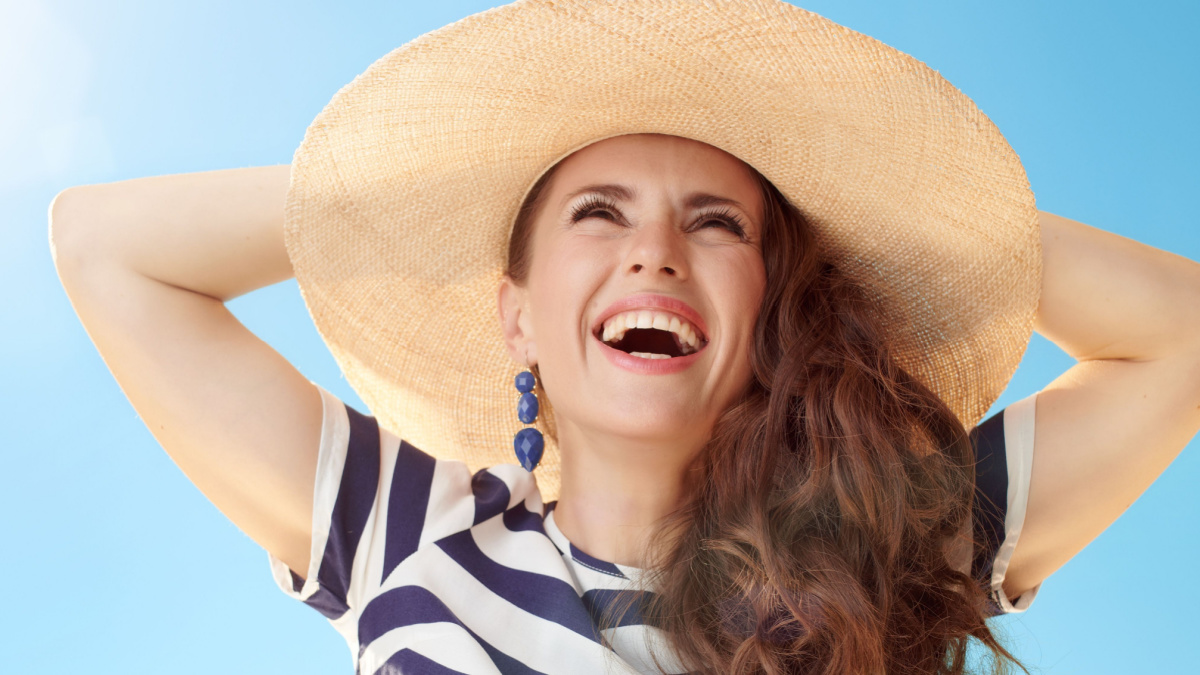 relaxed young woman in straw hat against blue sky looking up.