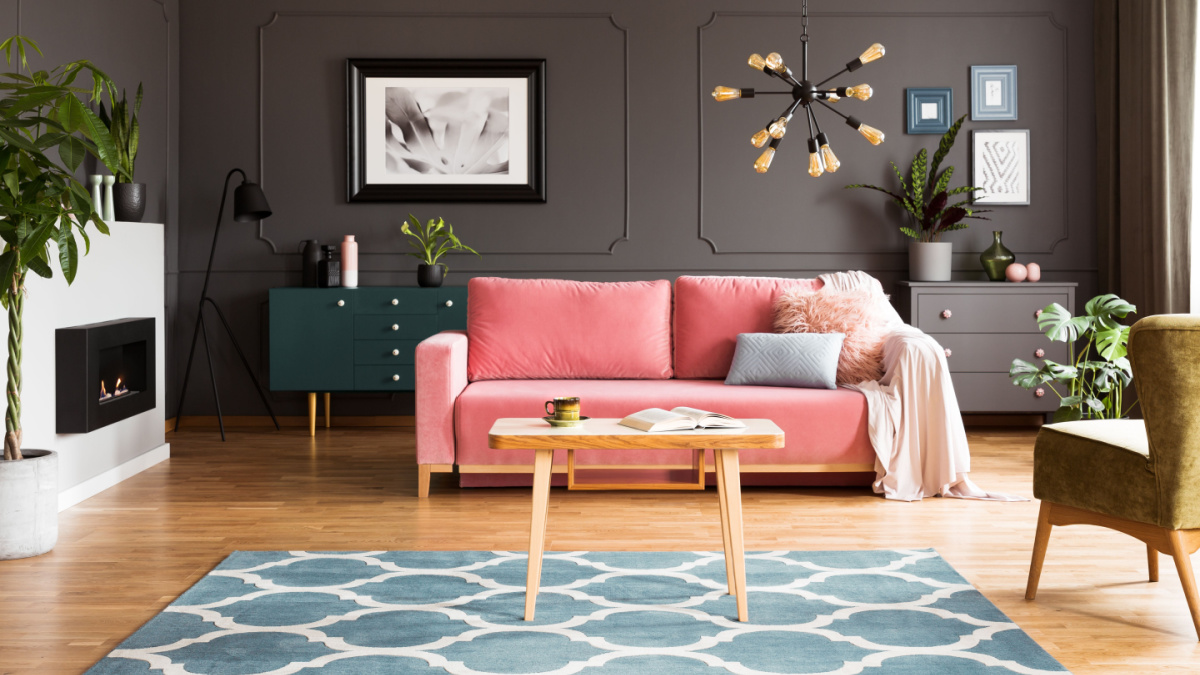 Wooden table on blue carpet in grey living room interior with fireplace and pink sofa.