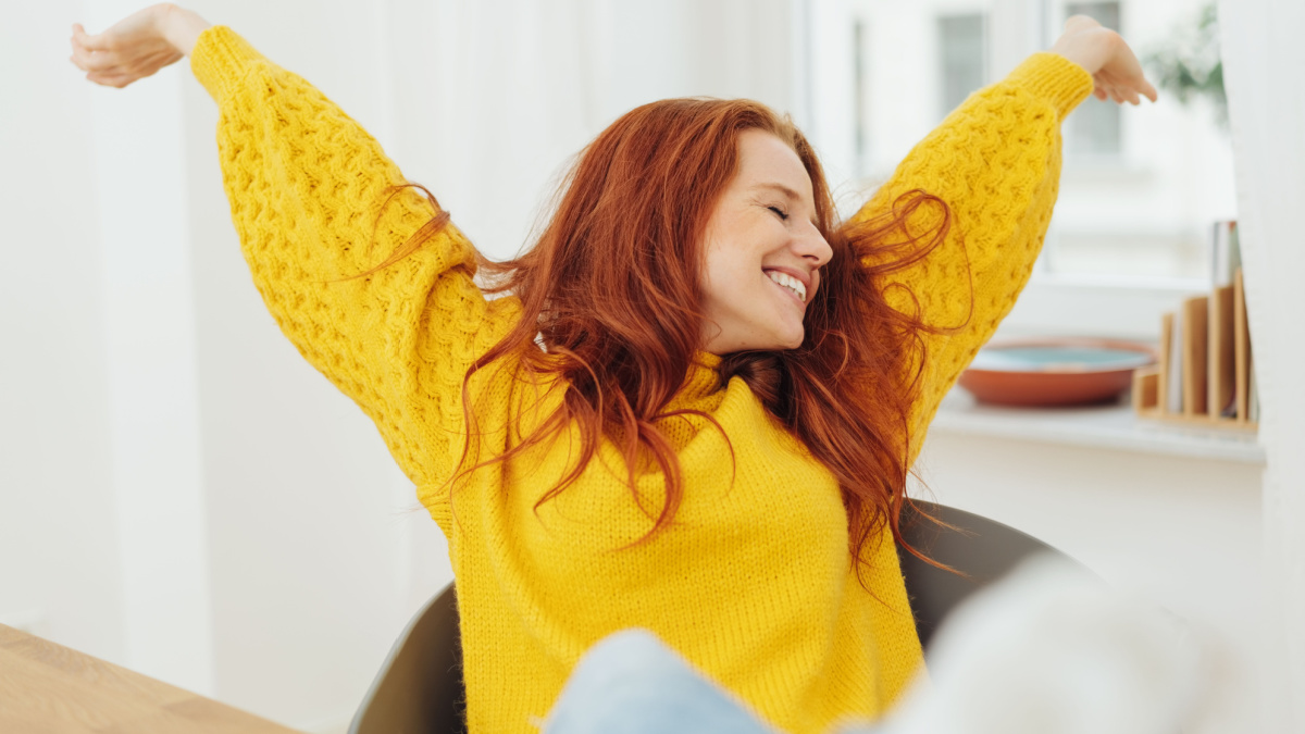 Happy pretty young woman stretching her arms as she leans back relaxing in her chair with a beaming smile.