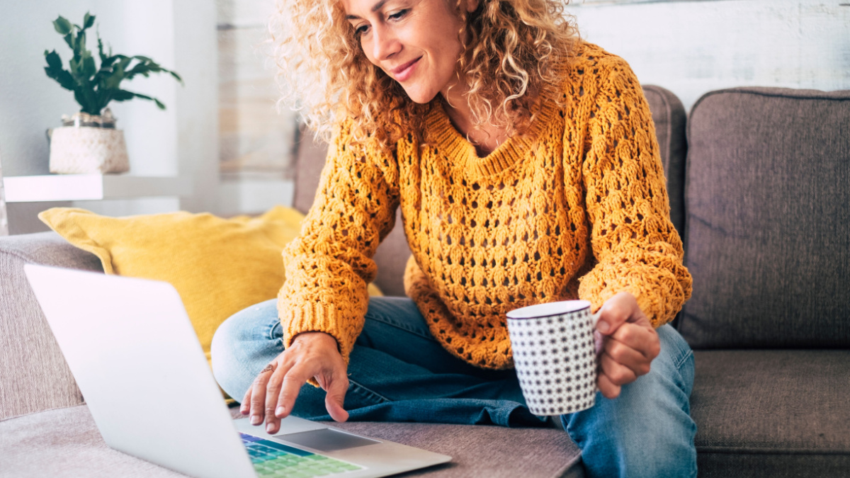 Nice beautiful lady with blonde curly hair work at the notebook sit down on the sofa at home - check on oline shops for cyber monday sales - technology woman concept for alternative office freelance.
