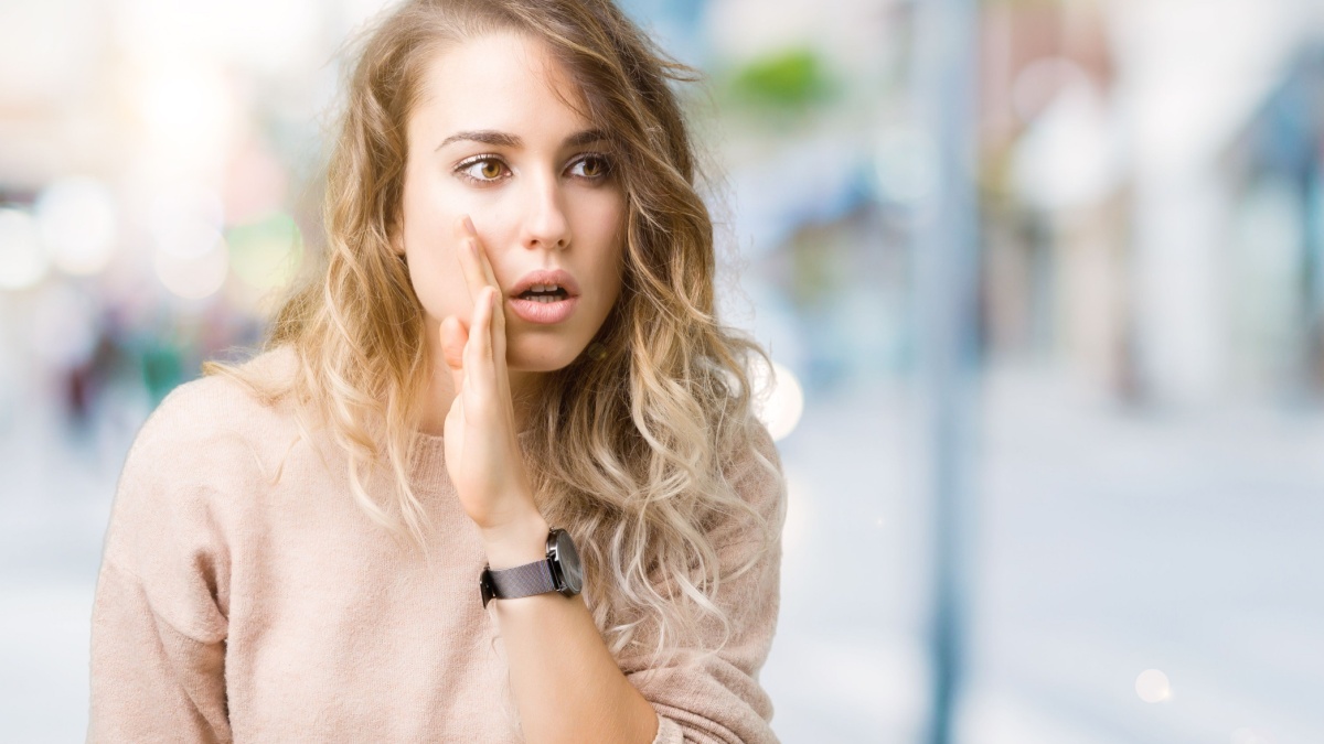 Beautiful young blonde woman wearing sweatershirt over isolated background hand on mouth telling secret rumor, whispering malicious talk conversation.