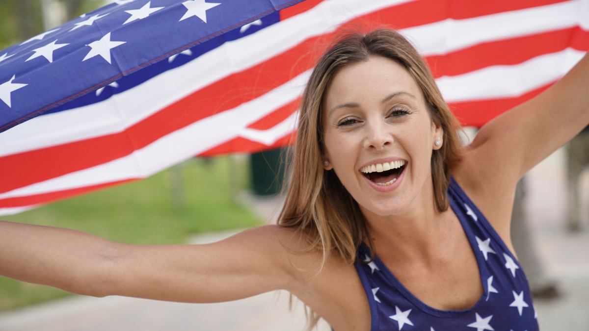 Proud attractive woman flying American flag outdoors.
