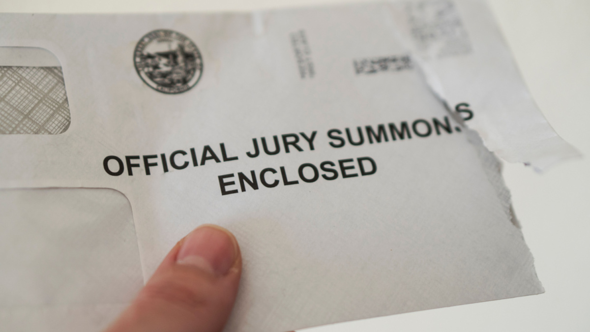 Closeup of open jury duty summons envelope, hand holding letter with white background, California juror receiving notice.