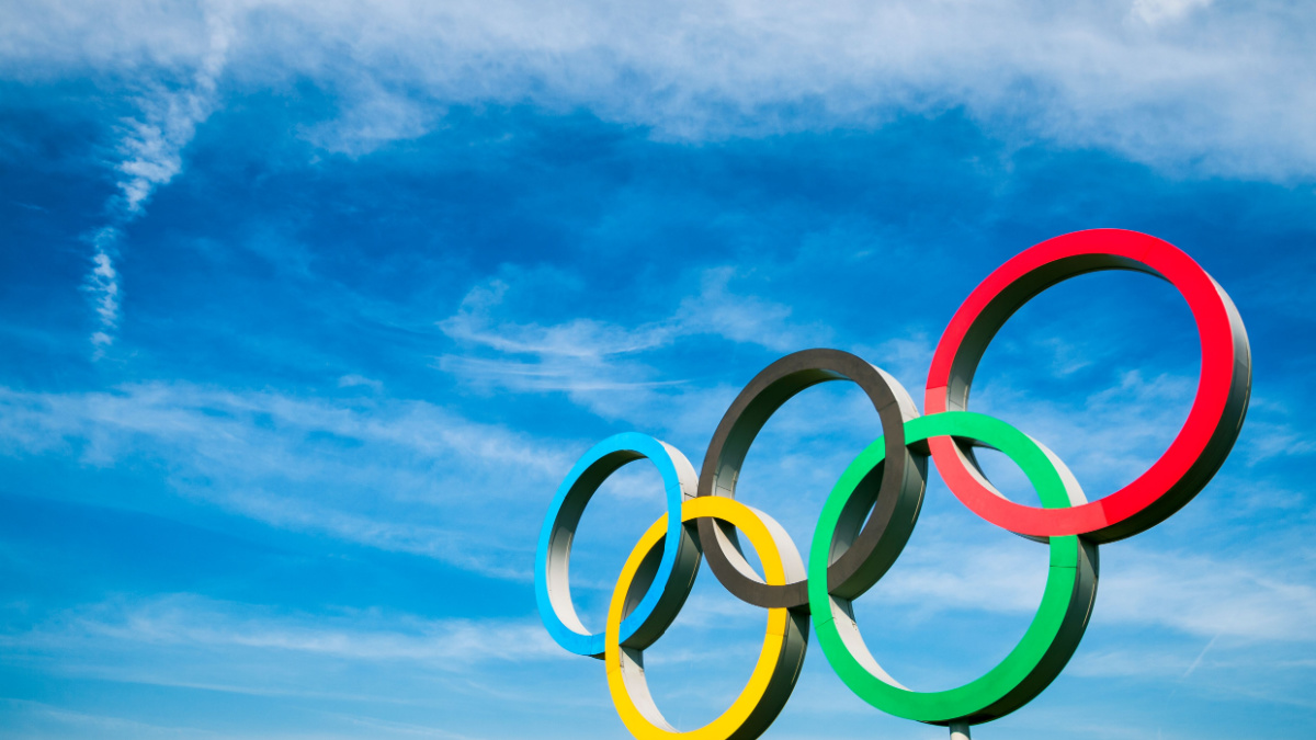 A large set of Olympic Rings stand under bright blue sky.