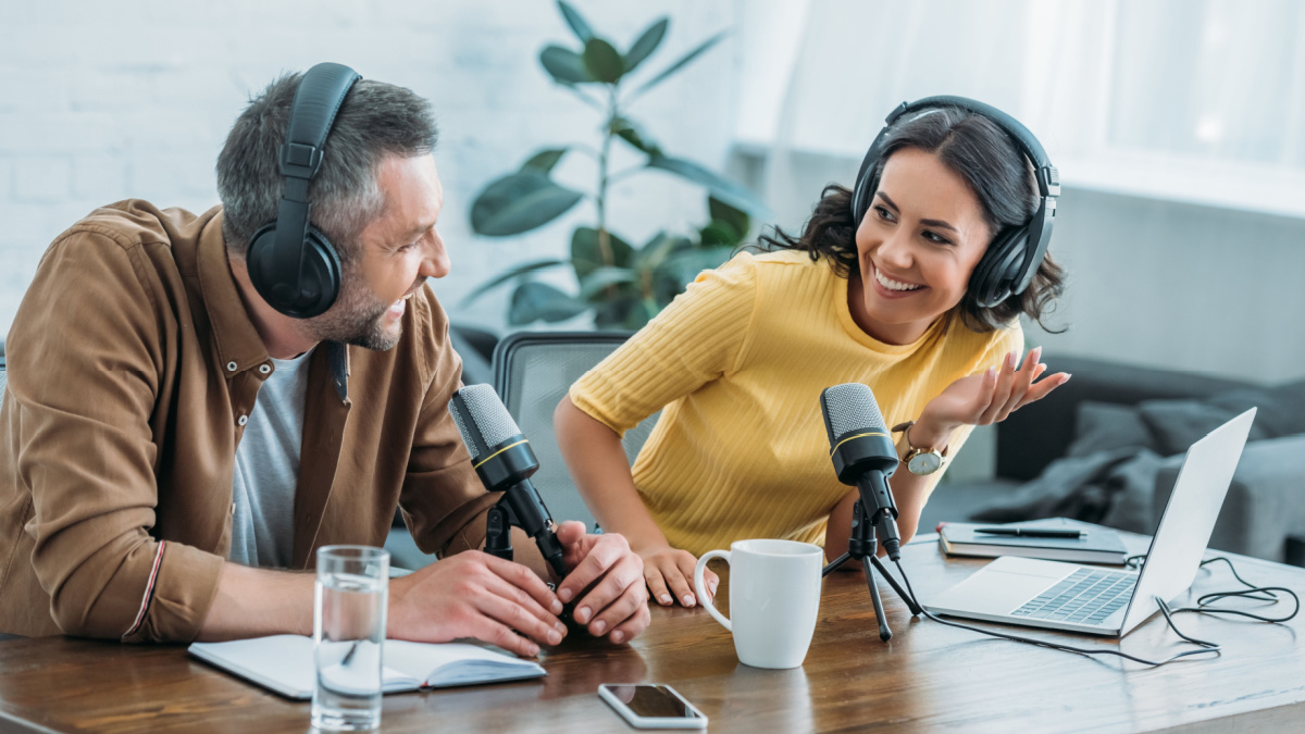 two radio hosts in headphones laughing while recording podcast in studio together