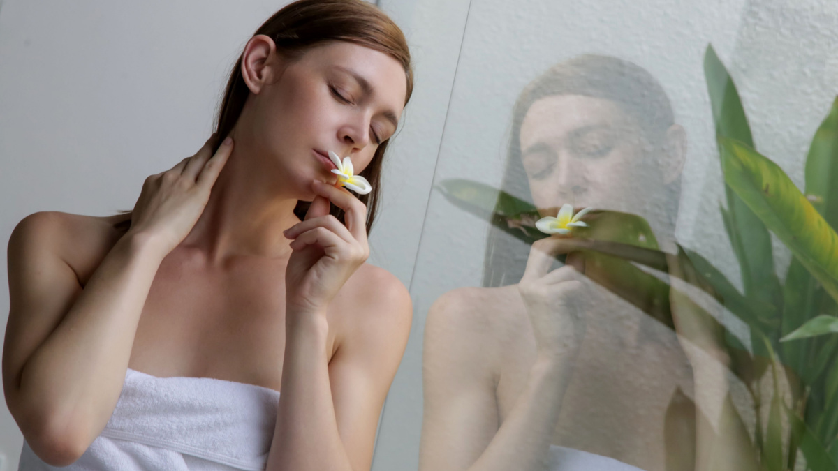 Portrait of a beautiful young woman in the bathroom, wearing a white towel and holding frangipani flower, relaxation and body care.