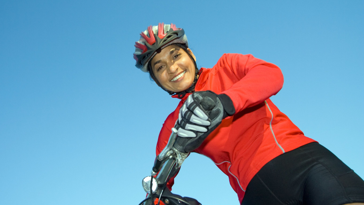 Close-up of woman standing next to bicycle, looking down and smiling. Wearing sports gear and helmet.