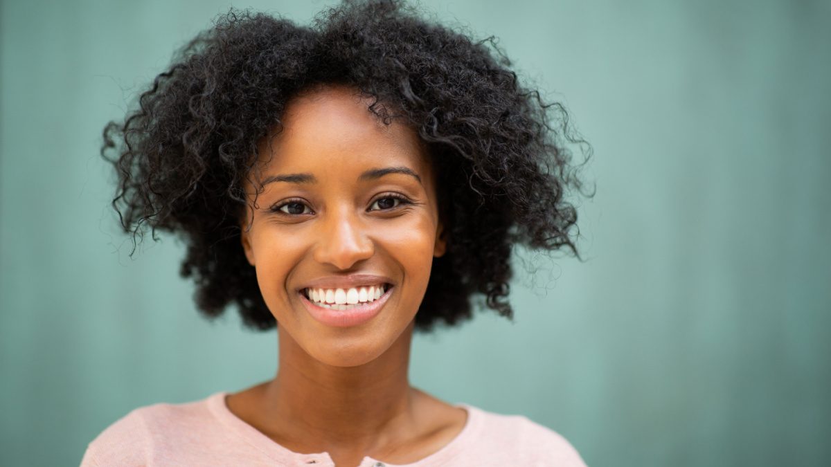 Close up horizontal portrait beautiful young black woman smiling by green background.